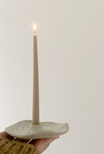 Charger l'image dans la galerie, Chandelle fine beige dans un bougeoir en céramique mouchetée aux contours irréguliers, tenu dans une main sur fond crème.