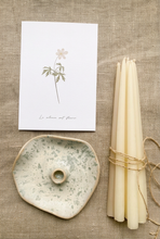 Charger l'image dans la galerie, Bougeoir en céramique mouchetée, chandelles fines ivoire nouées d’une ficelle et carte botanique, disposés sur du lin naturel.